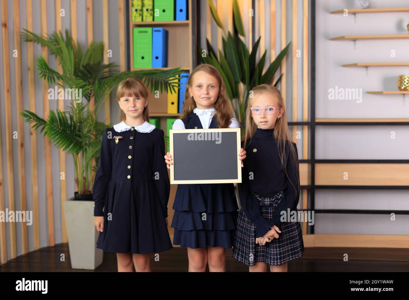 Drei Mädchen halten ein Reißbrett in einem Rahmen. Kinder halten einen Rahmen in den Händen. Schülerinnen halten eine Tafel mit Kreide. Stockfoto