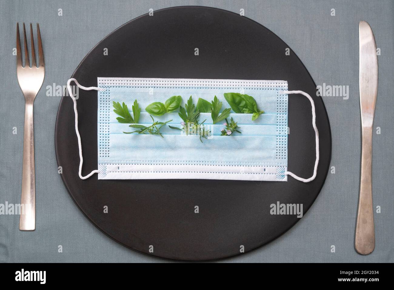 Aromatische Pflanzen in einer OP-Maske, auf einem schwarzen Teller, mit Gabel und Messer Stockfoto