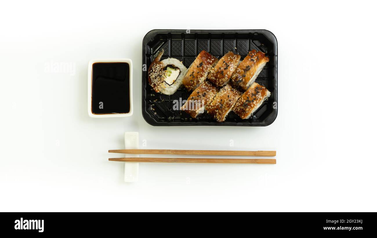 Sushi-Lieferkarton auf weißem Hintergrund. Japanisches Menü in schwarzer Transportbox mit Essstäbchen Stockfoto