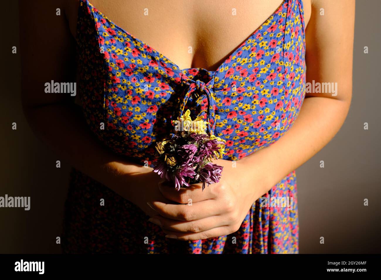 Frau trägt Blumenkleid hält verblasste Blume. Trauernde Frau mit Blumen. Gewalt gegen Frauen stoppen. Internationaler Frauentag Stockfoto
