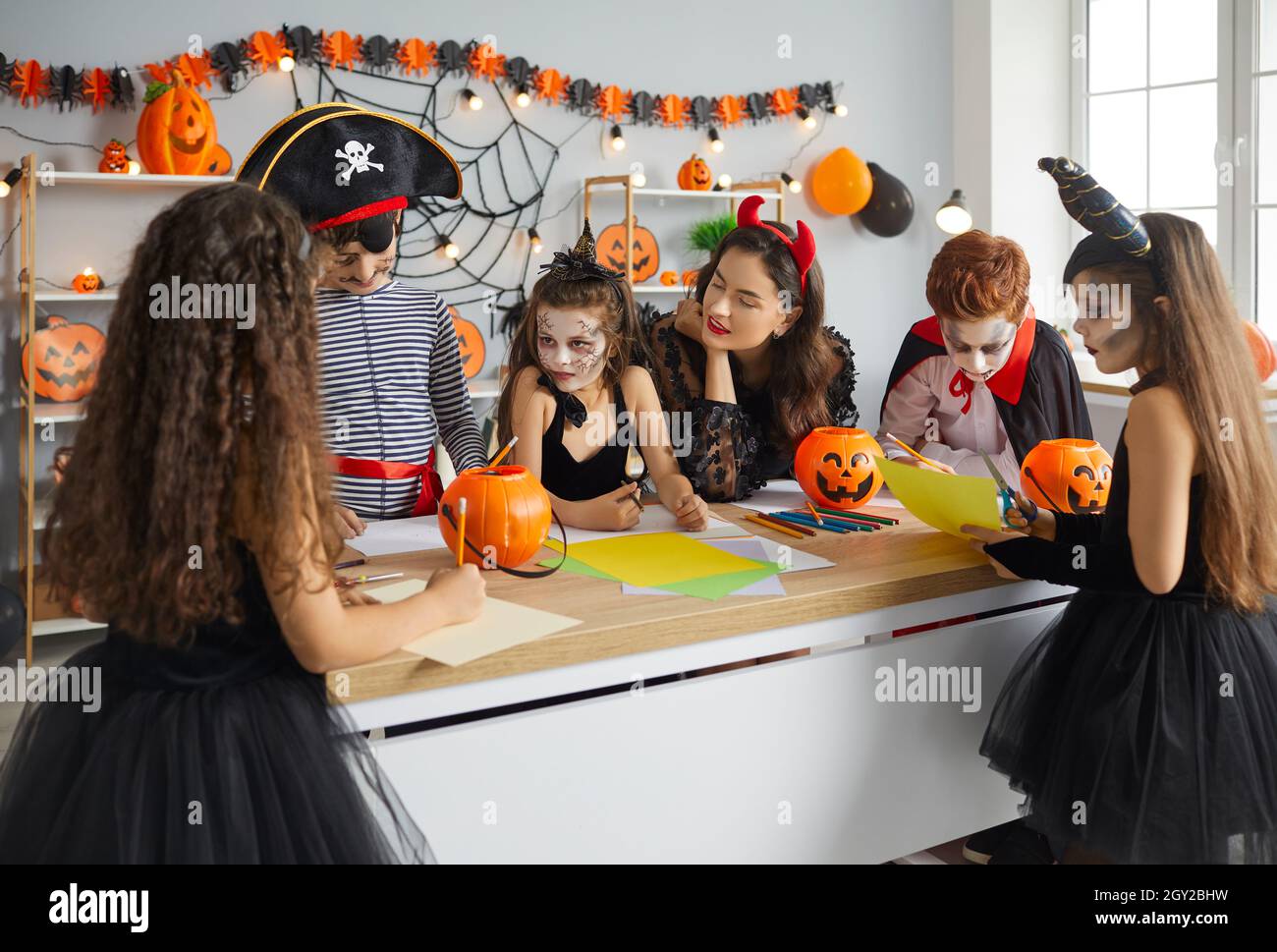 Gruppe von Kindern zusammen mit Frau bereitet handgemachte Halloween-Dekorationen aus Papier. Stockfoto
