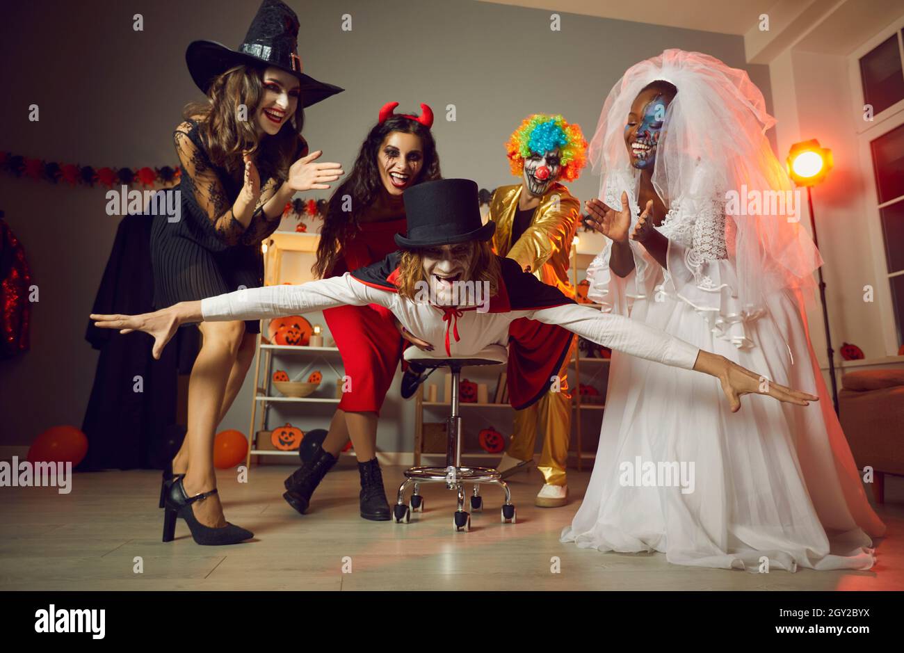 Fröhliche junge Menschen in gruseligen Kostümen, die auf der Halloween Party zu Hause verrückten Spaß haben Stockfoto