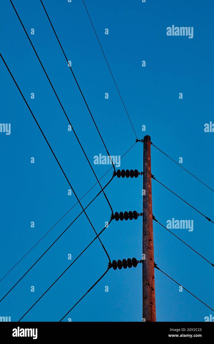 An einem klaren, blauen Himmel werden Stromleitungen an einem Telefonmast angeschlossen und umgeleitet Stockfoto