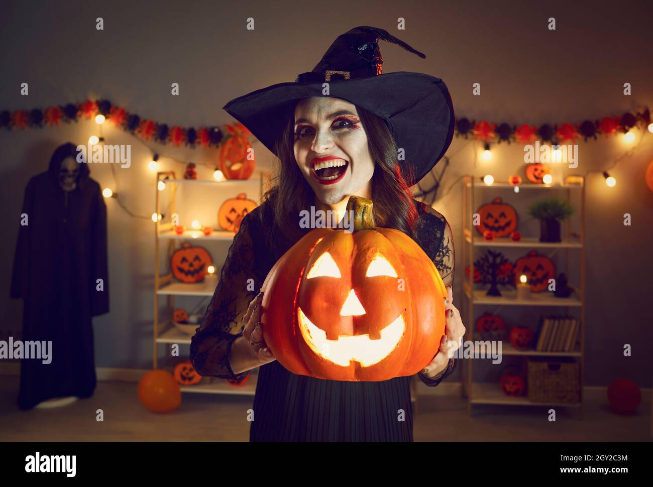 Halloween-Porträt der gruseligen und bösen Hexe mit glühenden Jack-o-Laterne in den Händen. Stockfoto