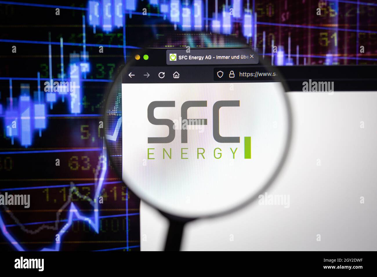 Firmenlogo von SFC Energy auf einer Website mit verschwommenen Börsenentwicklungen im Hintergrund, die auf einem Computerbildschirm durch eine Lupe gesehen werden Stockfoto