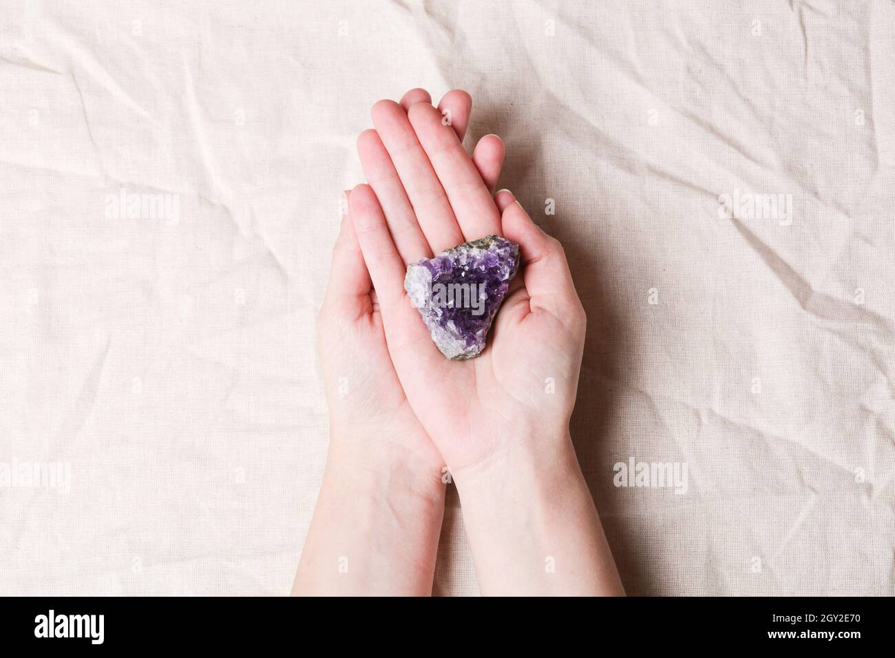 druse roher purpurner Amethyst-Kristall auf Stein auf Frau Hand auf grauem Leinen, magischer Fels für Ritual, Hexerei, spirituelle Praxis, Meditation Stockfoto