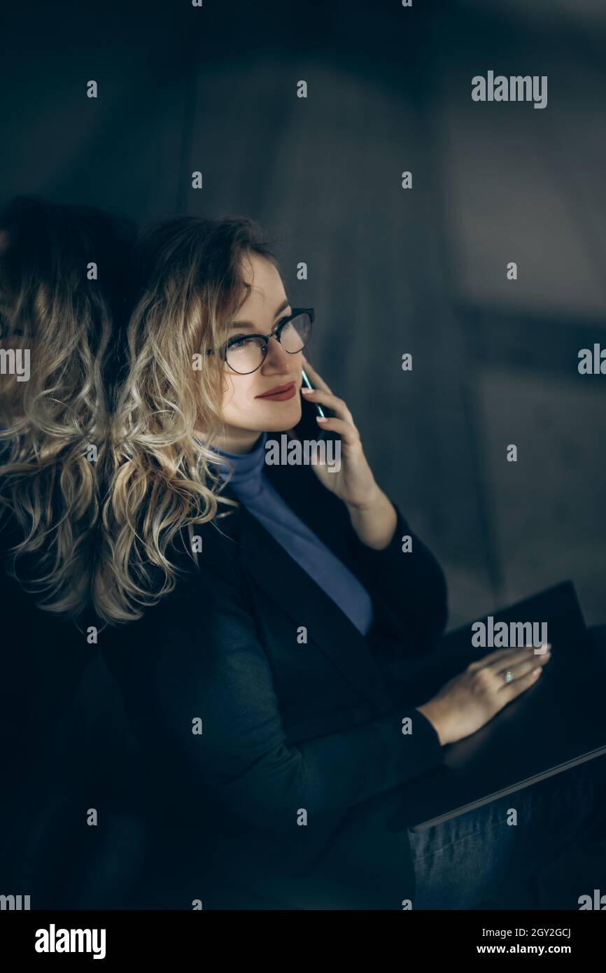 Schöne Geschäftsfrau mit Laptop auf den Knien spricht vom Smartphone. Stockfoto