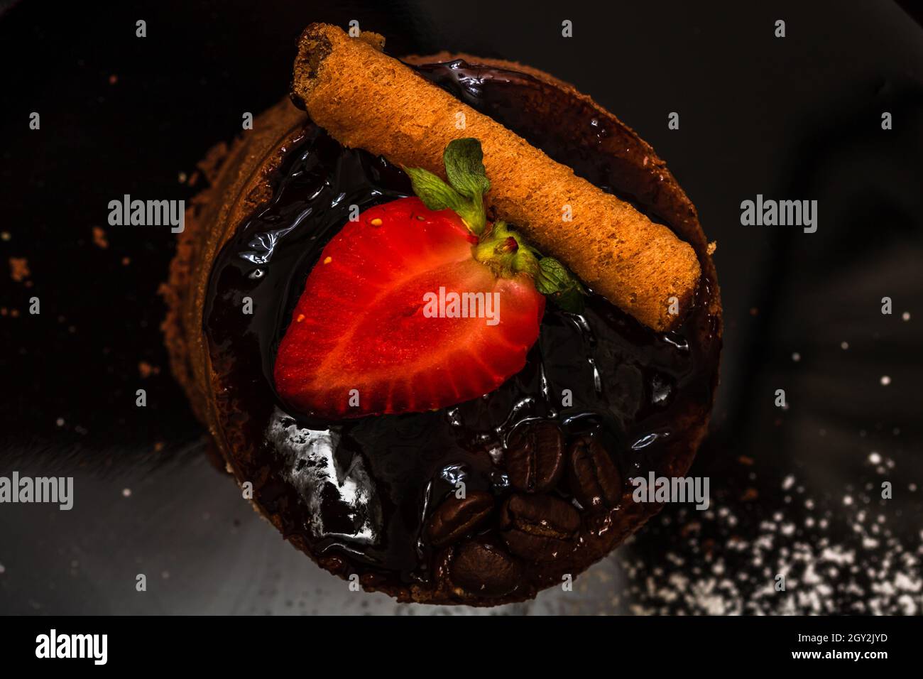 Nahaufnahme eines Schokoladenkuchens mit Zimt, Erdbeere in Scheiben und Schokoladenglasur oben Stockfoto