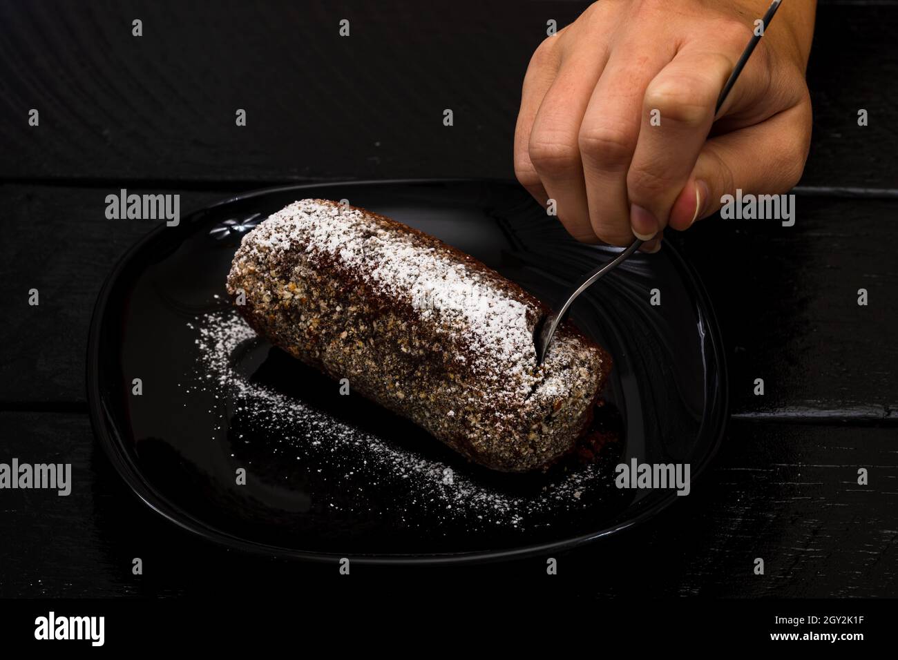 Nahaufnahme eines Mannes, der einen Schokoladenmehlkuchen auf einem schwarzen glasigen Tablett auf einem Holztisch forkert Stockfoto