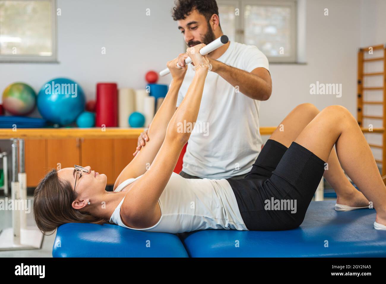Frau macht Übungen mit medizinischem Stab zur Stärkung ihrer Ellbogen und  Schultern mit Hilfe eines männlichen Physiotherapeuten Stockfotografie -  Alamy