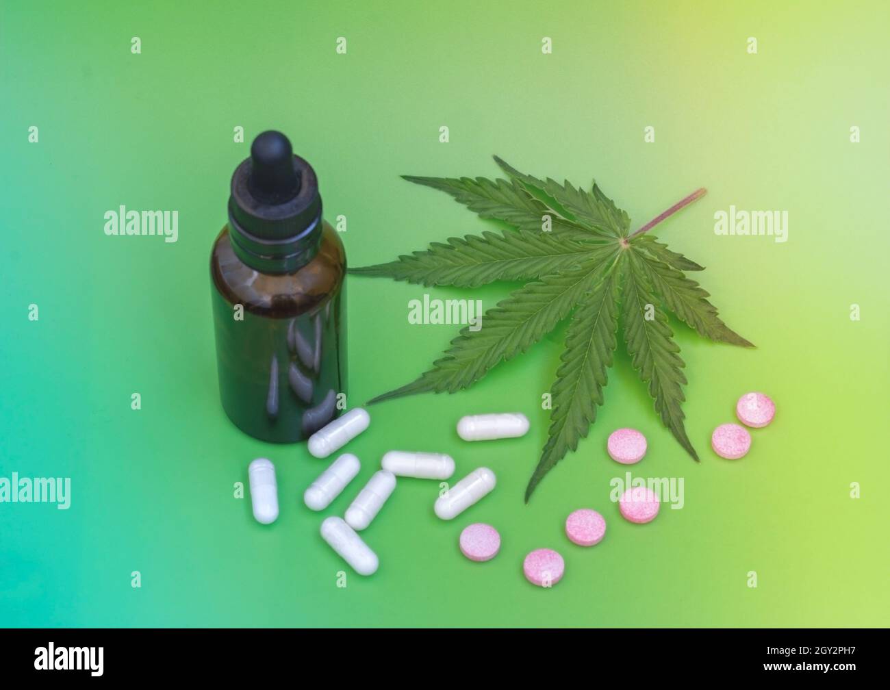 CBD-Pillen. Gruppe von CBD-Kapseln und rosa Cannabidiol-Pillen und Hanfblättern auf grünem Hintergrund. Verschiedene medizinische Cannabisprodukte. Medizinische Marijua Stockfoto