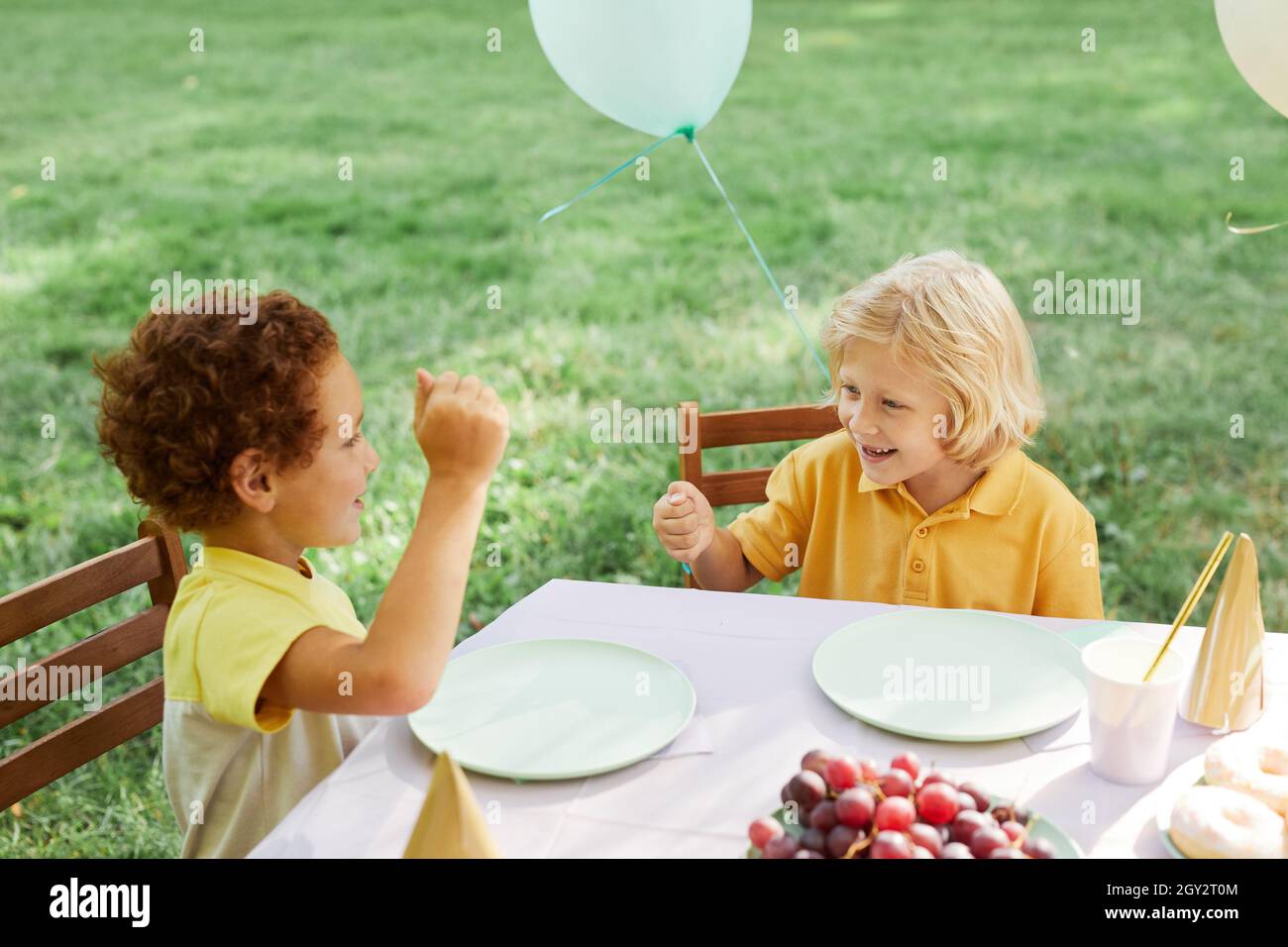 Zwei Kinder am Picknicktisch im Freien mit Luftballons für Geburtstagsfeier im Sommer geschmückt, kopieren Platz Stockfoto