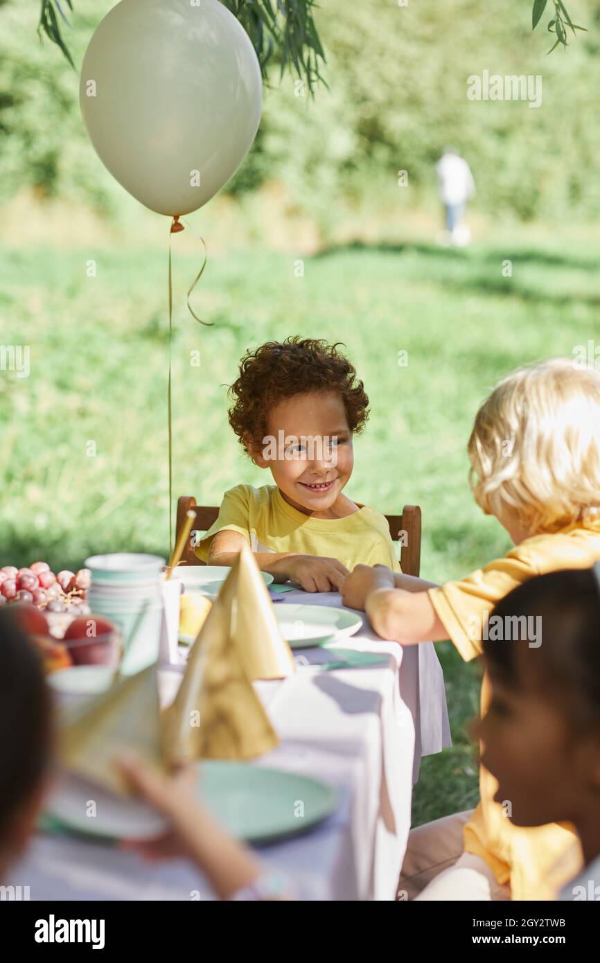 Verschiedene Gruppe von Kindern am Picknicktisch im Freien mit Ballons für Geburtstagsfeier im Sommer geschmückt Stockfoto