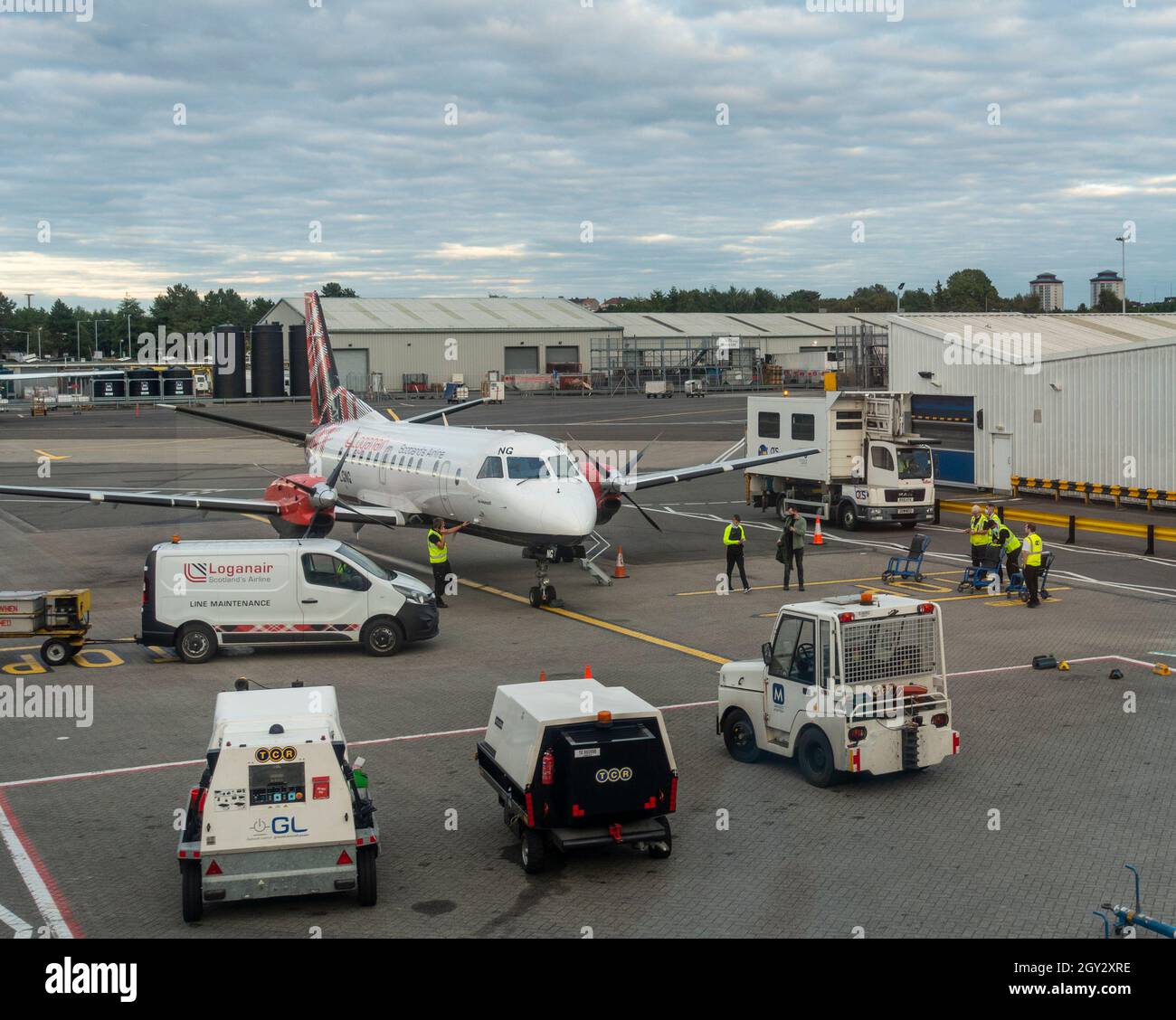 Unterstützung von Fahrzeugen und Mitarbeitern rund um ein Loganair Saab 340B Turboprop-Flugzeug reg. G-LGNG, das gerade am Flughafen Glasgow, Schottland, gelandet ist. Stockfoto