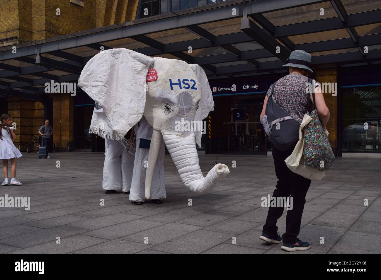 London, Großbritannien. August 2021. Demonstranten, die ein weißes Elefantenkostüm „HS2“ tragen, werden von einem Protestanten vor den Bahnhof geführt. Aktivisten versammelten sich vor dem Bahnhof King's Cross, um gegen das neue Hochgeschwindigkeits-2-Eisenbahnsystem (HS2) zu protestieren, das nach Meinung von Umweltschützern „ökologisch verheerend“ sein wird und den Steuerzahlern £170 Milliarden kosten wird. Stockfoto