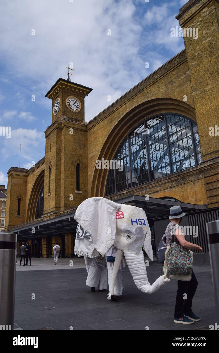 London, Großbritannien. August 2021. Demonstranten, die ein weißes Elefantenkostüm „HS2“ tragen, werden von einem Protestanten vor den Bahnhof geführt. Aktivisten versammelten sich vor dem Bahnhof King's Cross, um gegen das neue Hochgeschwindigkeits-2-Eisenbahnsystem (HS2) zu protestieren, das nach Meinung von Umweltschützern „ökologisch verheerend“ sein wird und den Steuerzahlern £170 Milliarden kosten wird. Stockfoto