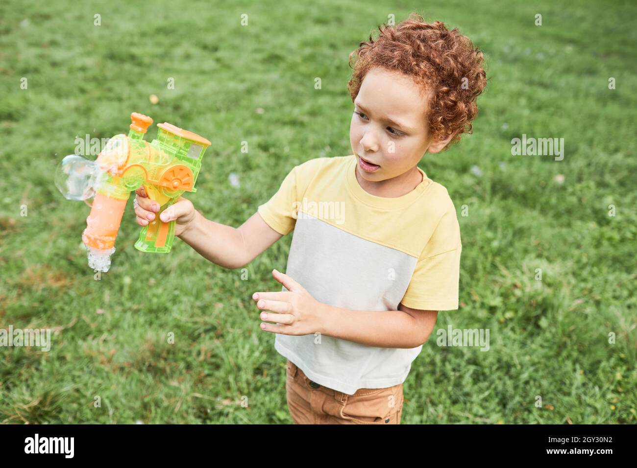 Porträt eines lockigen Jungen, der im Park mit einem Luftblasenspielzeug spielt, Kopierraum Stockfoto