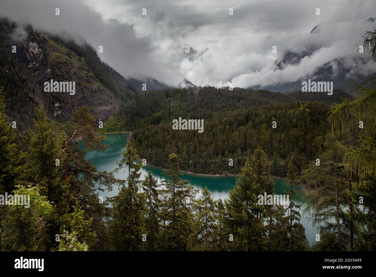 Birkenfarbener Bergsee mit einem dichten Wald um ihn herum und niedrigen Wolken darüber Stockfoto
