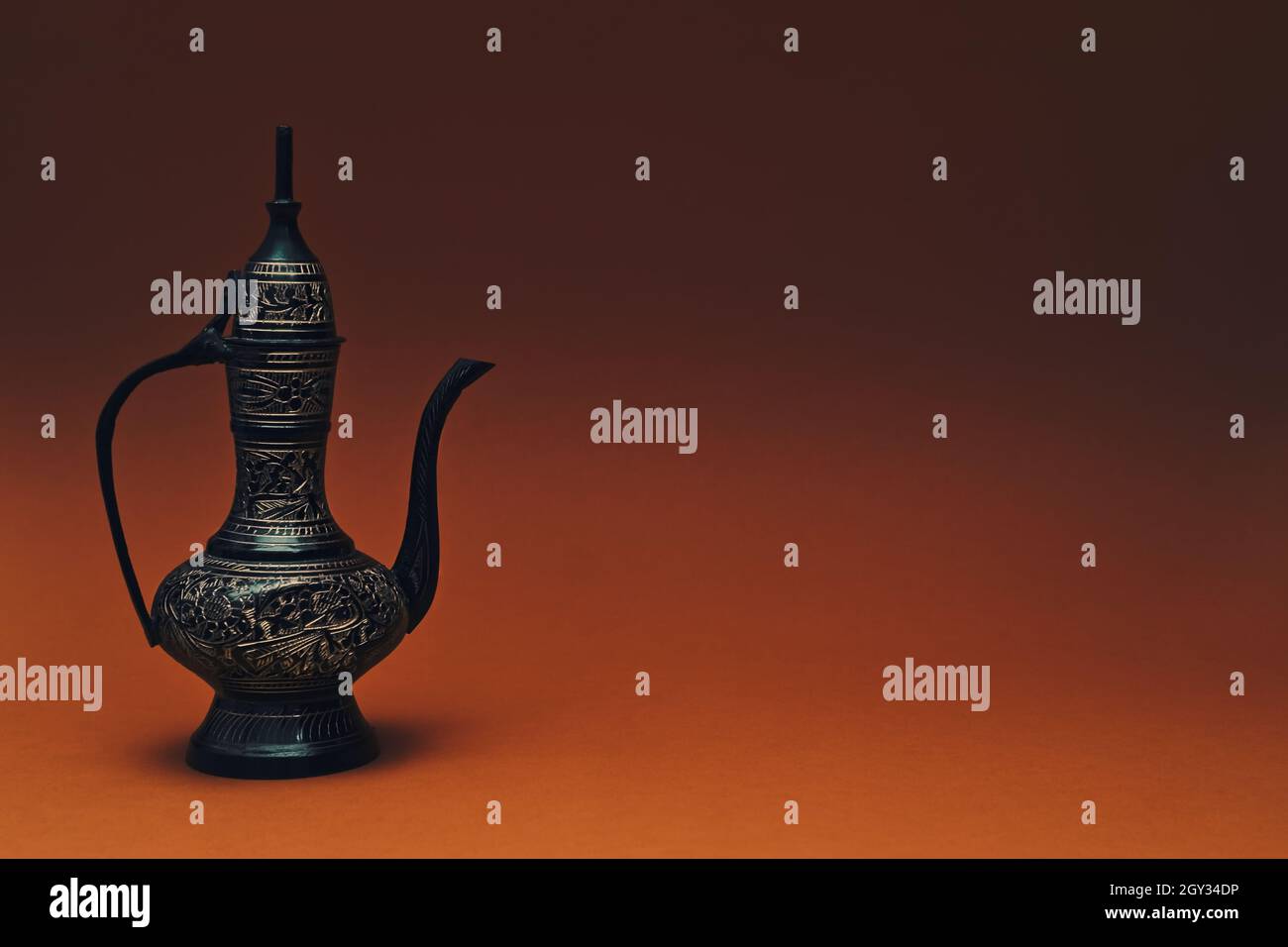 Vintage traditionelle islamische orientalische gravierte Kanne handgefertigt auf dunkelorangenen Hintergrund. Eleganter arabischer antiker großer Metallkrug, Kopierraum. Stockfoto