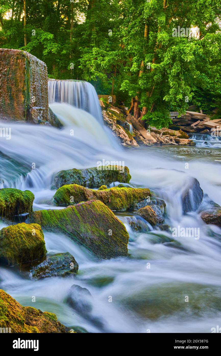 Algen bedecken kleine Felsen, die neben Wasserfällen und Steindamm aus dem Fluss ragen Stockfoto