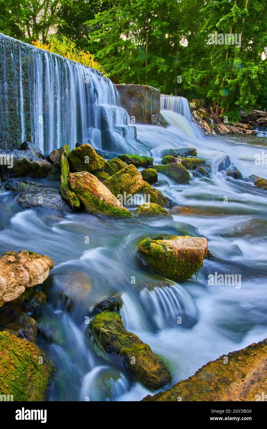 Algenfelsen ragen aus Wasserfällen aus dem von Menschen gemachten Damm heraus Stockfoto