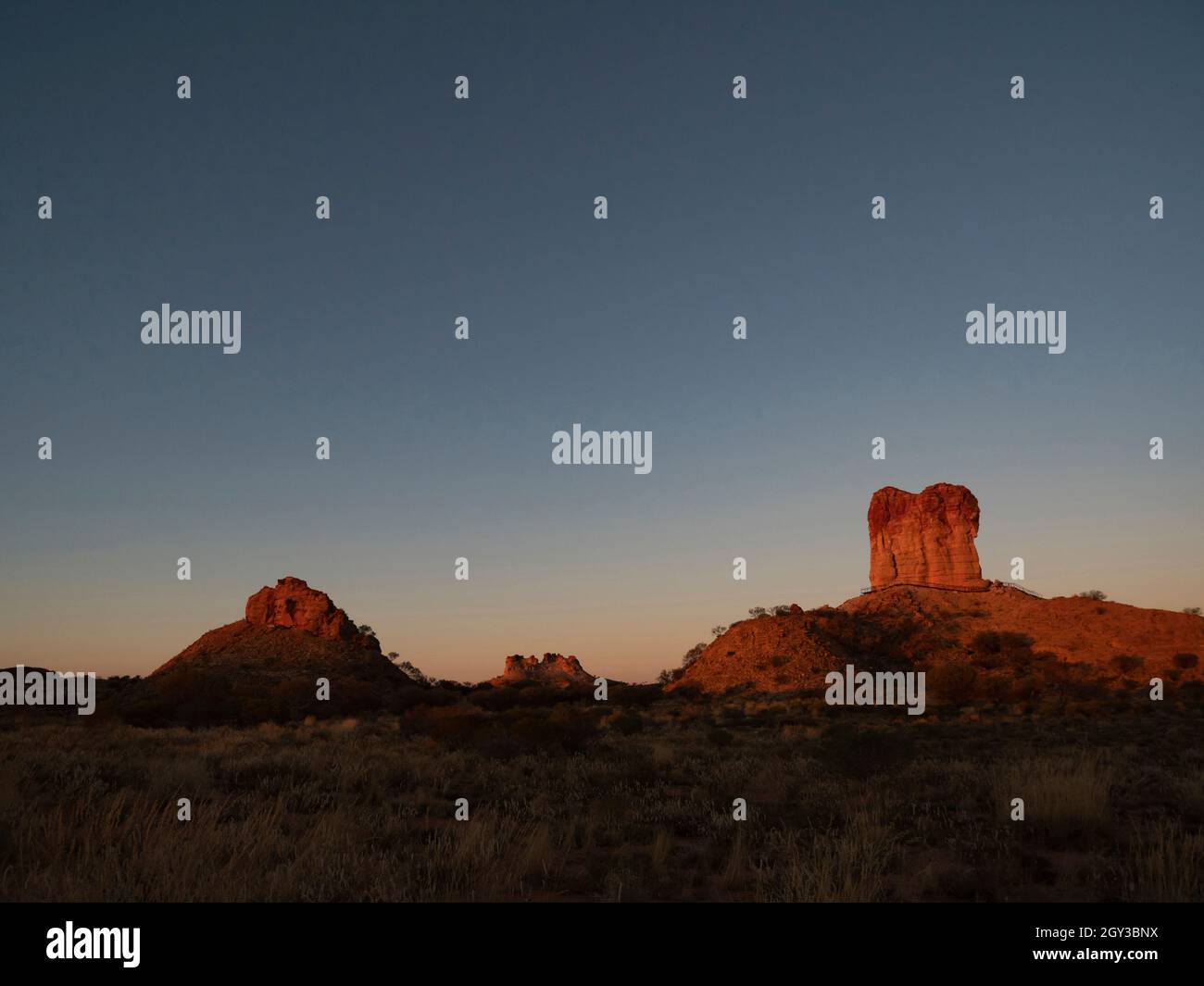 Chambers Pillar in der Nähe von Alice Springs in Zentralaustralien bei Sonnenuntergang mit rotem Sandstein und blauem Himmel Hintergrund mit Kopierraum. Stockfoto