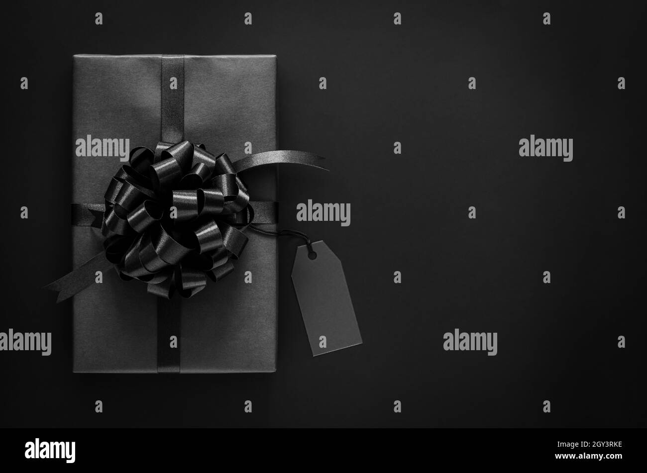 Eine schwarze Geschenkbox mit Band und leerem Preisschild setzt auf schwarzen Hintergrund. Black friday und Boxing Day Konzept. Stockfoto