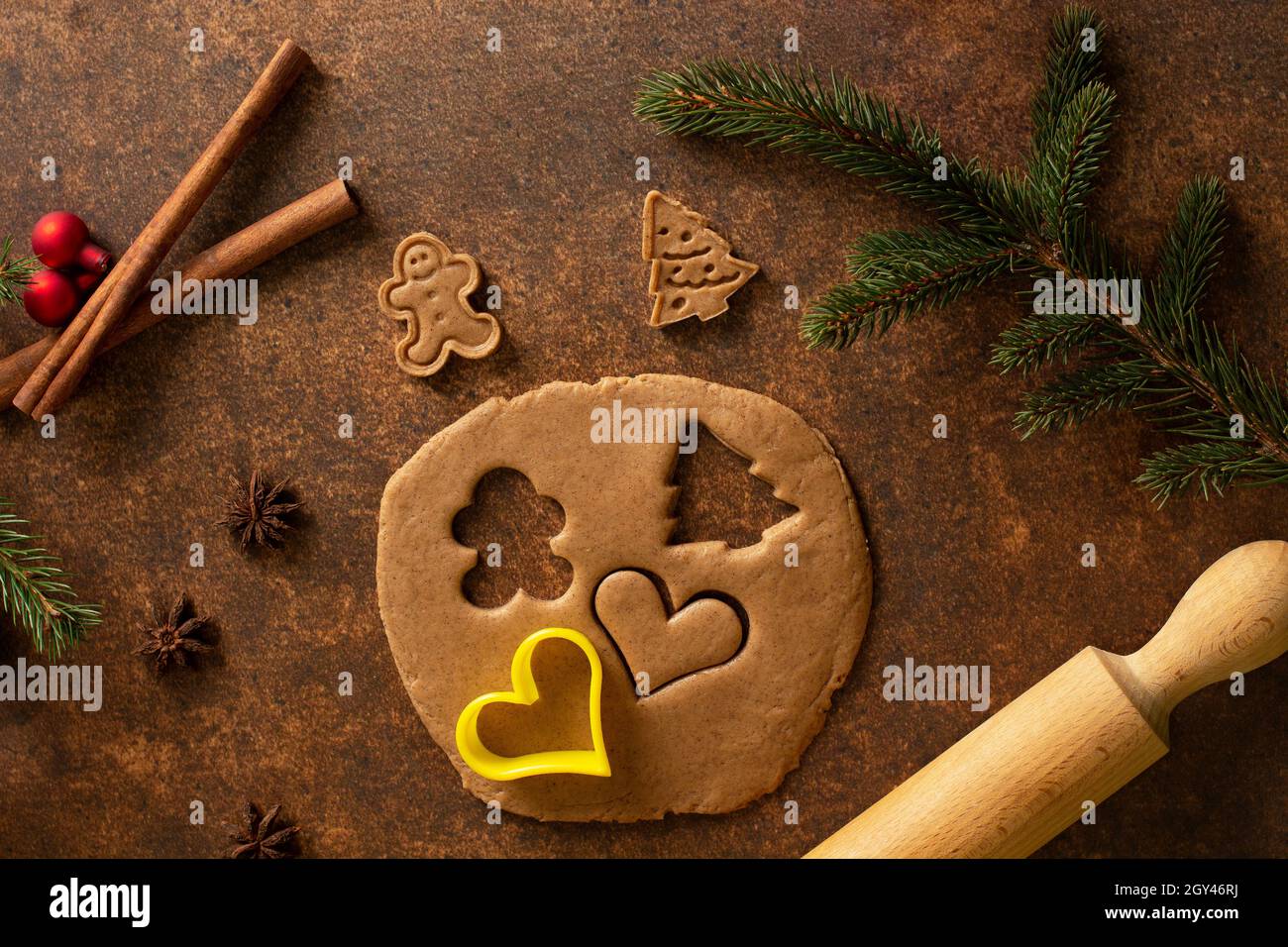 Lebkuchenteig, ausgerollt. Ein Lebkuchenmann, ein Weihnachtsbaum-Keks, ein Nudelholz, Zimtküllchen, Sternanisfrüchte, Weihnachtsbaumschmuck Stockfoto