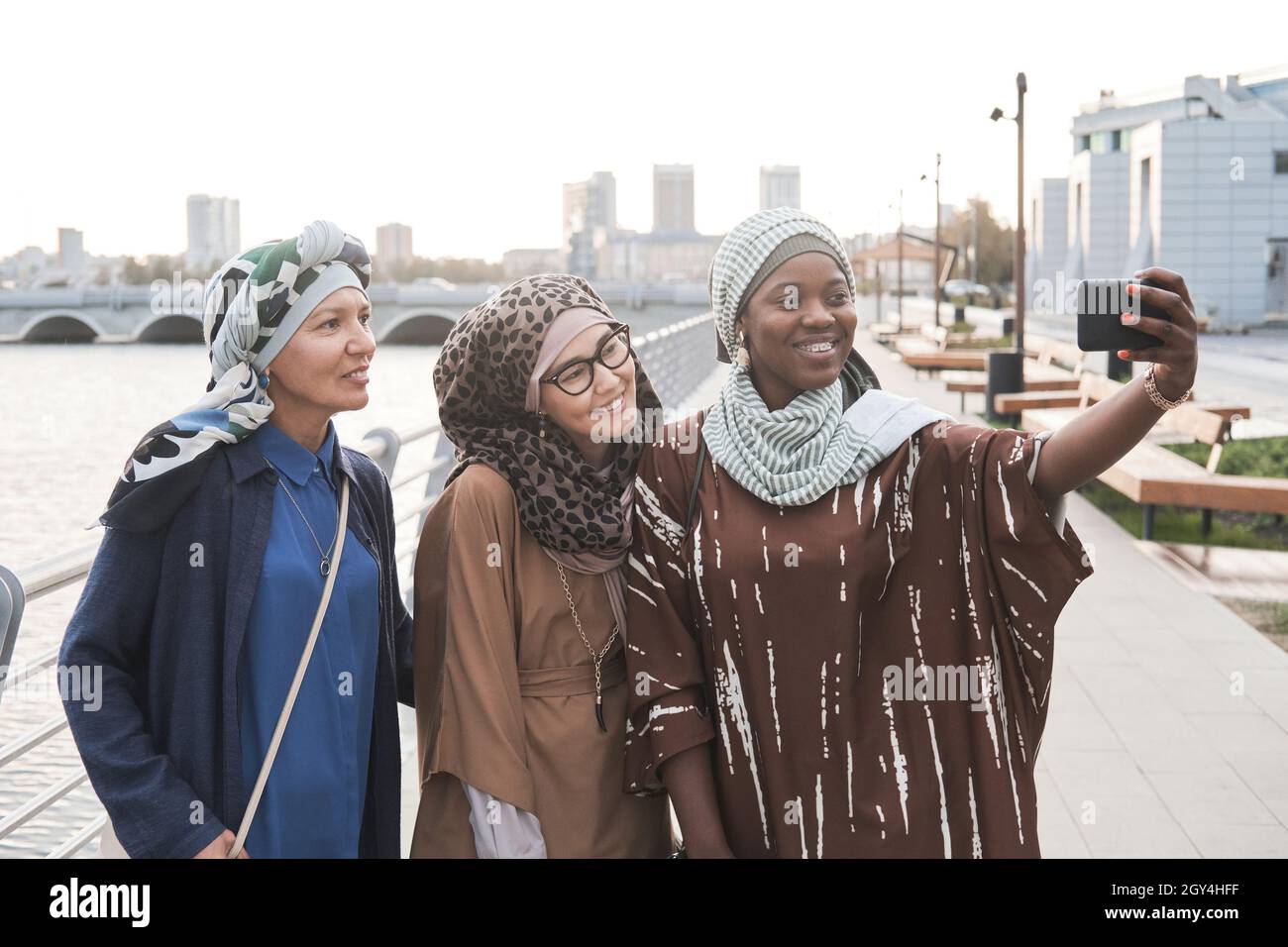 Eine Gruppe muslimischer Frauen, die die Kamera anlächeln, während sie Selfie auf dem Mobiltelefon machen, während sie in der Stadt stehen Stockfoto