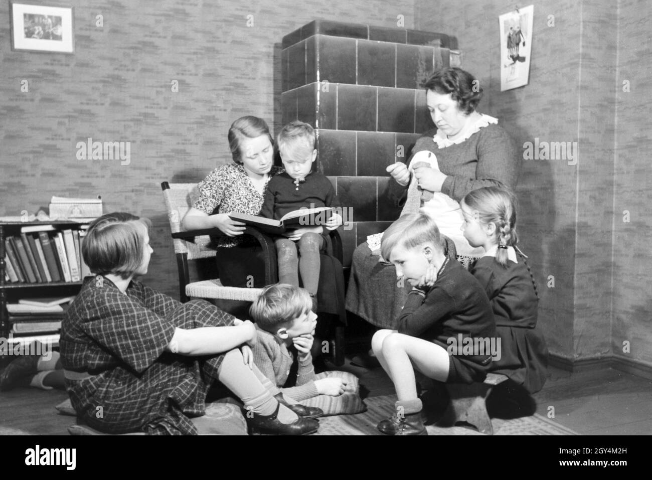 Mitglieder einer kinderreichen Familie lesen gemeinsam ein Buch, Deutsches Reich 30er Jahre. Mitglieder einer Großfamilie zusammen ein Buch lesen, Deutschland 1930. Stockfoto