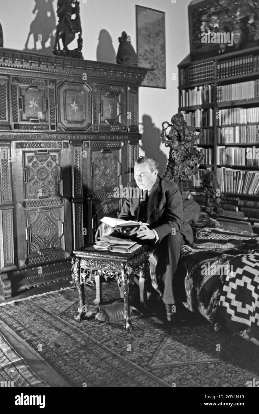 Der deutsche Mass Paul Wegener sitzt zu Hause in seiner Bibliothek und raucht eine Zigarre in Berlin, Deutschland, 1930er Jahre. Deutsche Schauspieler Paul Wegener das Rauchen einer Zigarre, während in der Bibliothek an seinem Haus in Berlin sitzen, Deutschland 1930. Stockfoto