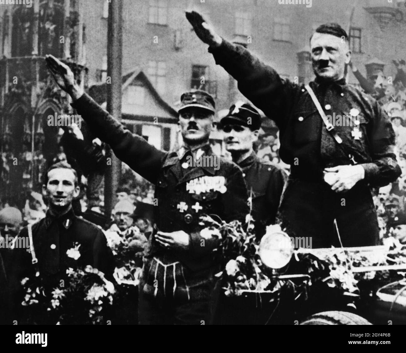 Hitler, Hess und Pfeffer begrüßen die Menge in Nürnberg mit dem Hitlergrüße aus dem Auto, das sich anlässlich des Reichsparteitags der NSDAP am schönen Brunnen auf dem Hauptmarkt versammelt hat. Hitler trägt die Parteiuniform wie üblich auf dem Reichsparteitag. [Automatisierte Übersetzung] Stockfoto