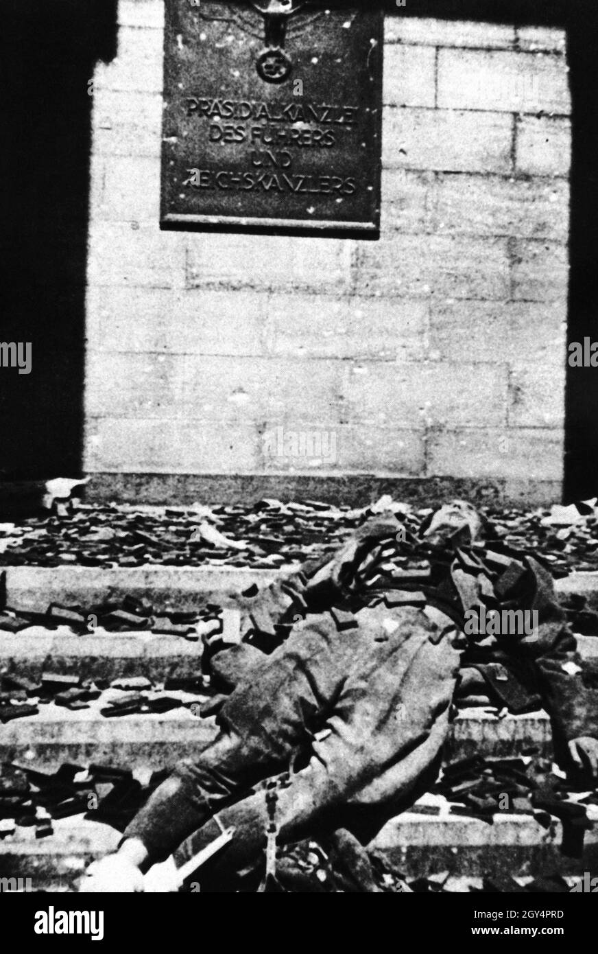 "Unmittelbar nach dem Ende der Kämpfe um Berlin machte ein sowjetischer Kriegsfotograf dieses Bild eines deutschen Offizierskörpers, der mit Nazi-Abzeichen bedeckt war, vor einem Eingang zur Reichskanzlei mit der Tafel ''Präsidentenkanzlei des Führers und Reichskanzlers''. [Automatisierte Übersetzung]' Stockfoto