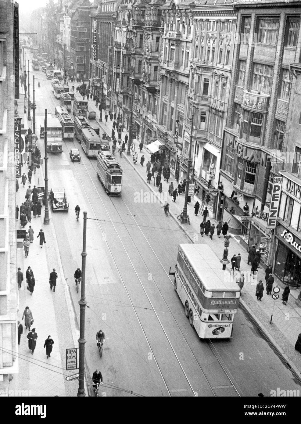 „Busse und Straßenbahnen fahren am 25. Januar 1938 auf der Leipziger Straße in Berlin-Mitte. Der Frontbus wirbt mit „Continental Tyres“. Der Blick geht von der Friedrichstraße in Richtung Mauerstraße und Leipziger Platz. Die Straße ist mit Geschäften gesäumt, darunter ''S. Rader Pelze'', ''Montblanc'', ''Hess und Rom Möbel'', eine Parfümerie, ''Herz Röcke'', eine ''Berlitz School'' (rechte Straßenseite) und ein ''J. Schröder'' Shop neben dem Hotel Kempinski (links von der Straße). [Automatisierte Übersetzung]' Stockfoto