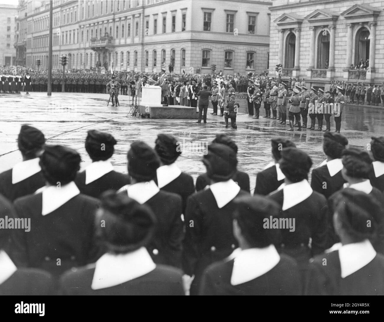 Adolf Hitler (Mitte) hält am 16. Juni 1937 eine Rede vor 1200 italienischen jungen Faschisten der Opera Nazionale Balilla (Jugendorganisation der italienischen Faschisten). Hinter ihm auf dem Wilhelmplatz in Berlin-Mitte stehen Menschen der NSDAP, der SA und der italienischen faschistischen Organisationen. Zuvor war die Parade durch die Wilhelmstraße gezogen. Fotografen auf dem Platz Filmen und fotografieren Adolf Hitler. Im Hintergrund rechts die Neue Reichskanzlei, links das Reichsverkehrsministerium. [Automatisierte Übersetzung] Stockfoto