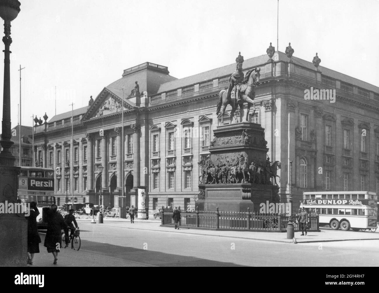 Passanten gehen 1936 an der Straße unter den Linden in Berlin-Mitte vorbei an der Reiterstatue Friedrichs des Großen. Dahinter steht die Staatsbibliothek Berlin. Auf den Doppeldeckerbussen sind Anzeigen für ''peril''' und den Slogan ''Drive DUNLOP Tyres'' zu sehen. [Automatisierte Übersetzung]' Stockfoto