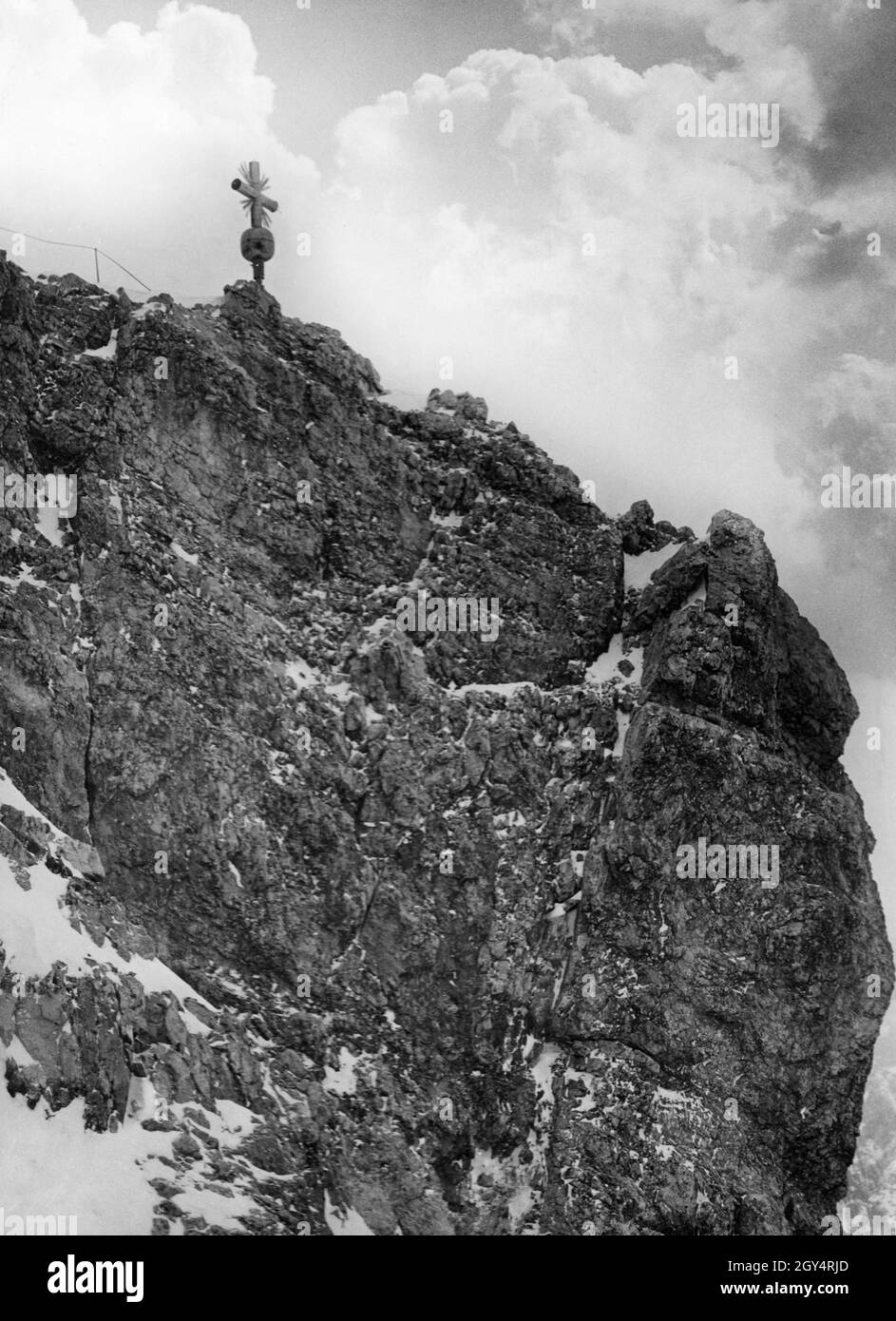 Der Aufstieg ist auf den letzten Metern bis zum Gipfelkreuz auf der Zugspitze steil. Wie links vom Kreuz zu sehen ist, wurde der Weg bereits 1935 mit einem Seil gesichert. [Automatisierte Übersetzung] Stockfoto