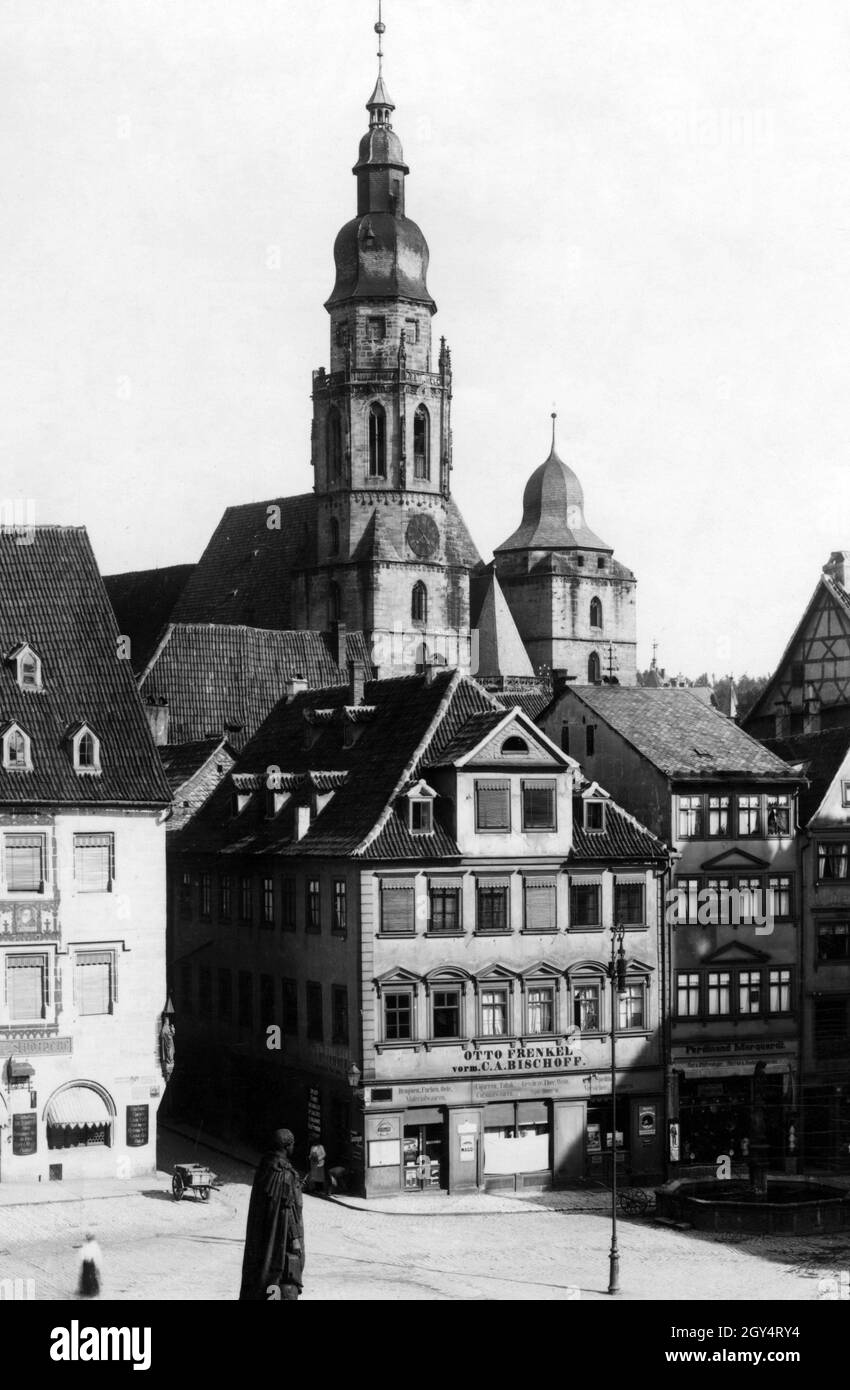 'Das Foto von 1933 zeigt den Marktplatz mit Prinz-Albert-Denkmal in Coburg und die Morizkirche im Hintergrund. Links von der Steingasse befindet sich das Haus mit der Hofapotheke, die 1543 gegründet wurde. Auf der rechten Seite der Gasse, der Besitzer ''Otto Frenkel vorm. C.A. Bischoff“ verkauft unter anderem „Teppiche, Farben, Öle, Materielle Güter, Zigarren, Tabak, Kolonialwaren'. Daneben befindet sich das Modehaus 'Ferdinand Marquardt' mit ''Mützen und Mützen' und 'Männerbekleidung und Jungenbekleidung''. [Automatisierte Übersetzung]' Stockfoto