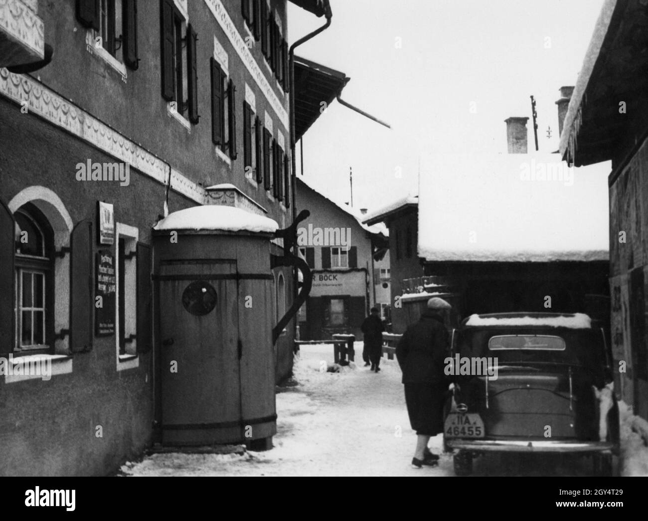 Am 6. Februar 1936, dem Eröffnungstag der Olympischen Winterspiele, wird in einer Seitenstraße in Garmisch-Partenkirchen ein Auto aus München (Kennzeichen II A) geparkt. An der façade des Hauses links war eine Tür in Form eines biersteins angebracht, die in den Gasthof führte. Stockfoto