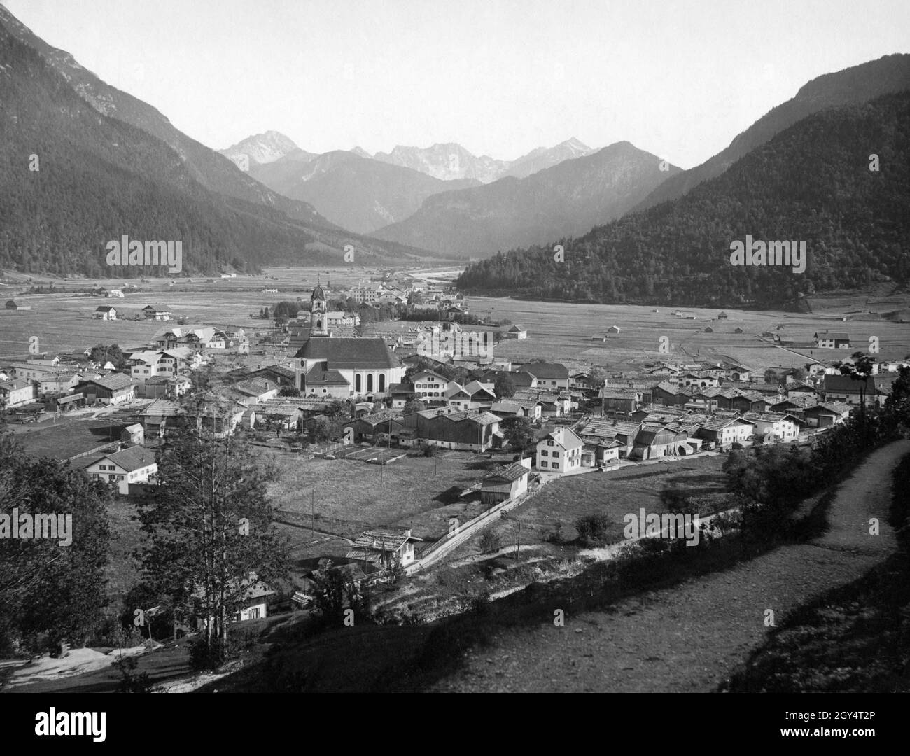 Der Blick geht über Mittenwald mit der Pfarrkirche St. Peter und Paul im Zentrum in Richtung Tiroler Berge bei Seefeld im Süden. [Automatisierte Übersetzung] Stockfoto