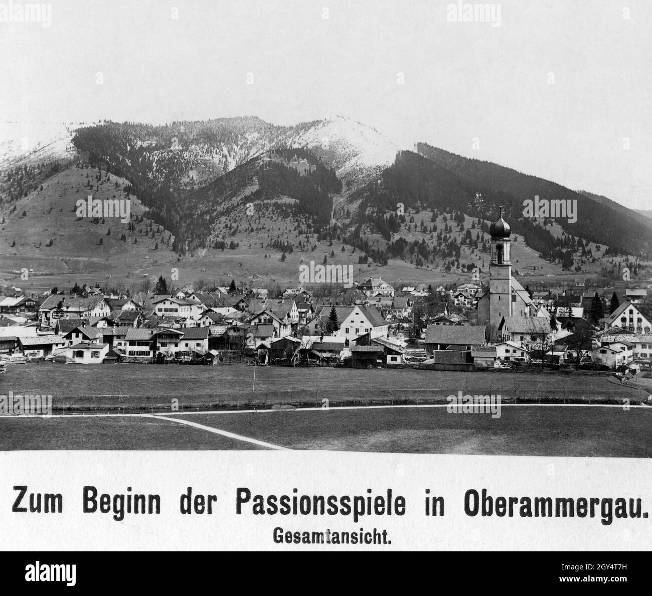 1922 fand das für 1920 geplante Passionsspiel in Oberammergau statt. Der Blick geht über die Ammer und das Zentrum von Oberammergau mit der Kirche St. Peter und Paul nach Osten zum Gschwandkopf und Großen Aufacker, dessen Gipfel leicht eingeschneit sind. [Automatisierte Übersetzung] Stockfoto