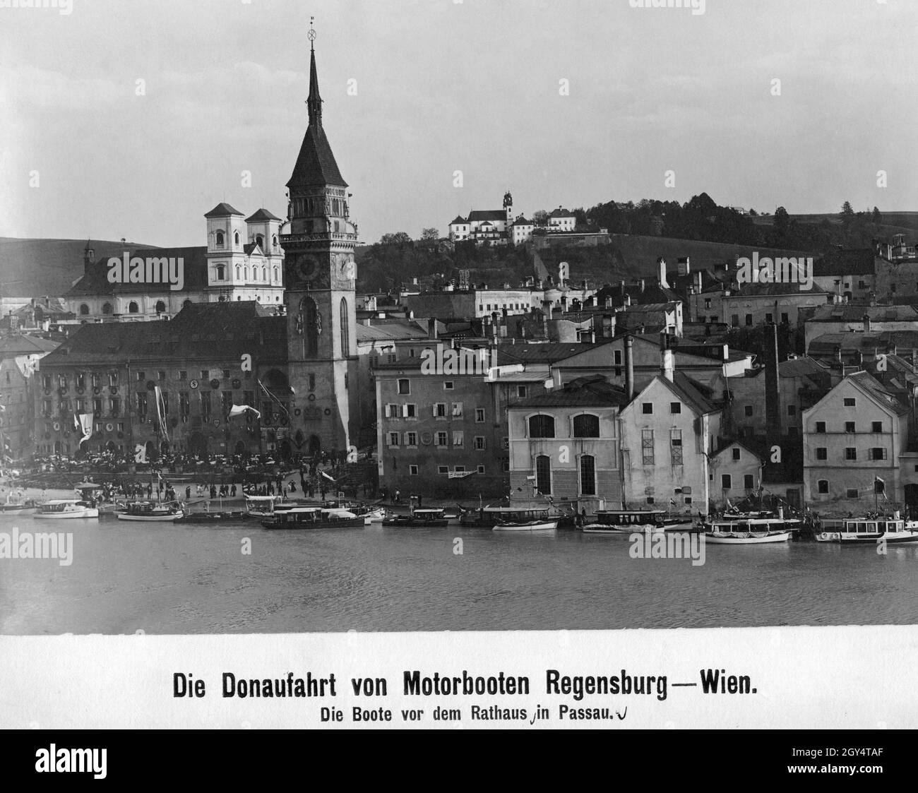 Im Jahr 1909 fand eine Donaukreuzfahrt von Regensburg nach Wien statt. Die teilnehmenden Motorboote haben auf diesem Foto am Donaukai in Passau angedockt. Auf dem Rathausplatz vor dem Rathausturm haben sich Menschen versammelt. Im Hintergrund ist die Kirche St. Michael (links) und das Kloster Mariahilf über der Innstadt zu sehen. [Automatisierte Übersetzung] Stockfoto