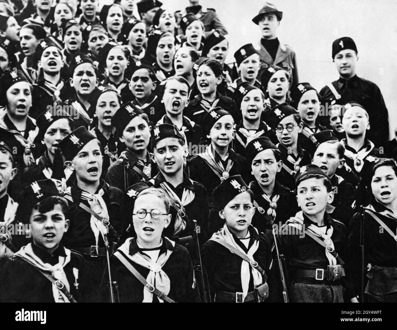 Um den Waffenstillstandstag zu feiern, wurden 1935 in Italien große Paraden abgehalten. Zahlreiche Einheiten der faschistischen Jugendorganisation Opera Nazionale Balilla nahmen daran Teil. Auf dem Bild steht eine Gruppe von Balilla-Jungen auf einer Tribüne und singt ein Lied. [Automatisierte Übersetzung] Stockfoto