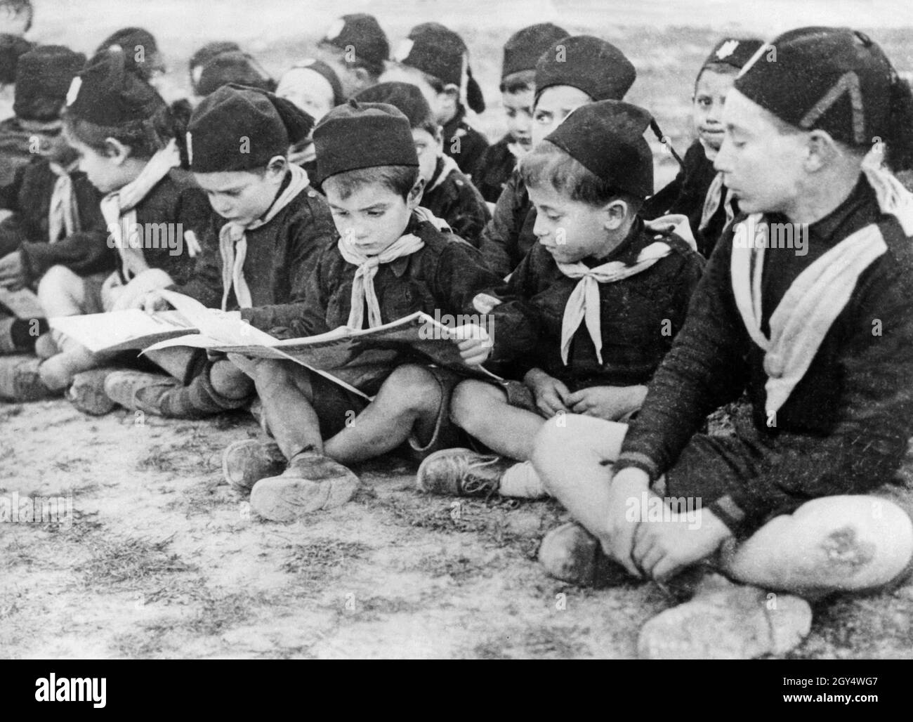 "Sogar kleine Kinder wurden vom faschistischen Regime in Italien in die Jugendorganisation Opera Nazionale Balilla integriert, um sie für ihre eigene Ideologie mitnehmen zu können. Die jüngsten Jungen im Alter von sechs bis acht Jahren waren die sogenannten "Figli della lupa". Auf dem Bild vom 1. Januar 1931 ist eine kleine Gruppe dieser "Figli" im Farnesina Training Center zu sehen, das sich im römischen Stadtteil Farnesina befindet. Sie schauen sich große Bilderbücher und Broschüren an. [Automatisierte Übersetzung]' Stockfoto