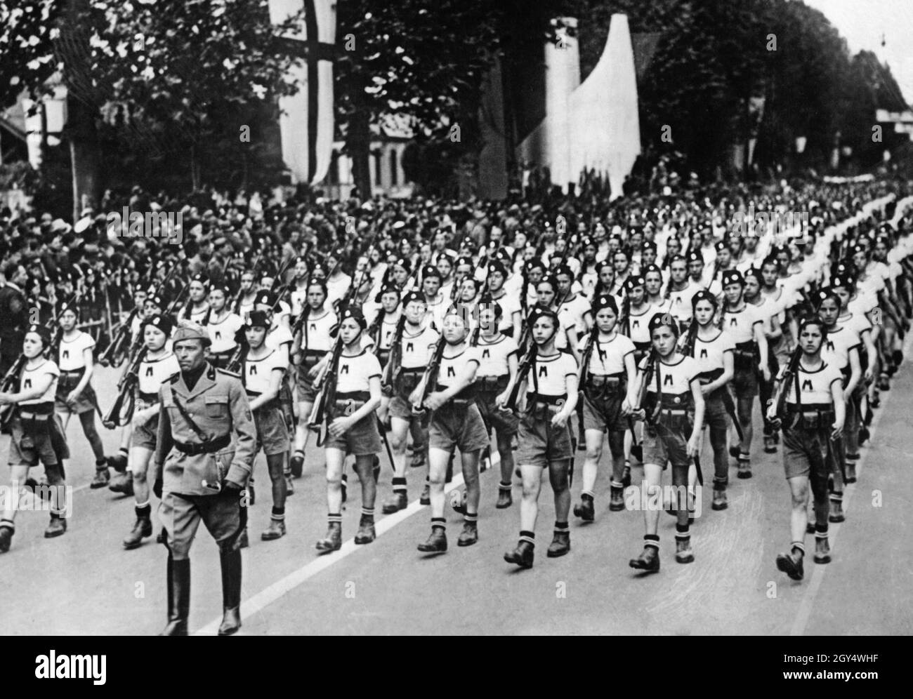 Unter der Leitung eines Gruppenleiters der Opera Nazionale Balilla marschiert Anfang Juni 1938 eine Gruppe von Jugendlichen in einer Parade durch die Straßen Mailands. Sie tragen einheitliche Kleidung, Gewehre und Patronenbeutel. [Automatisierte Übersetzung] Stockfoto