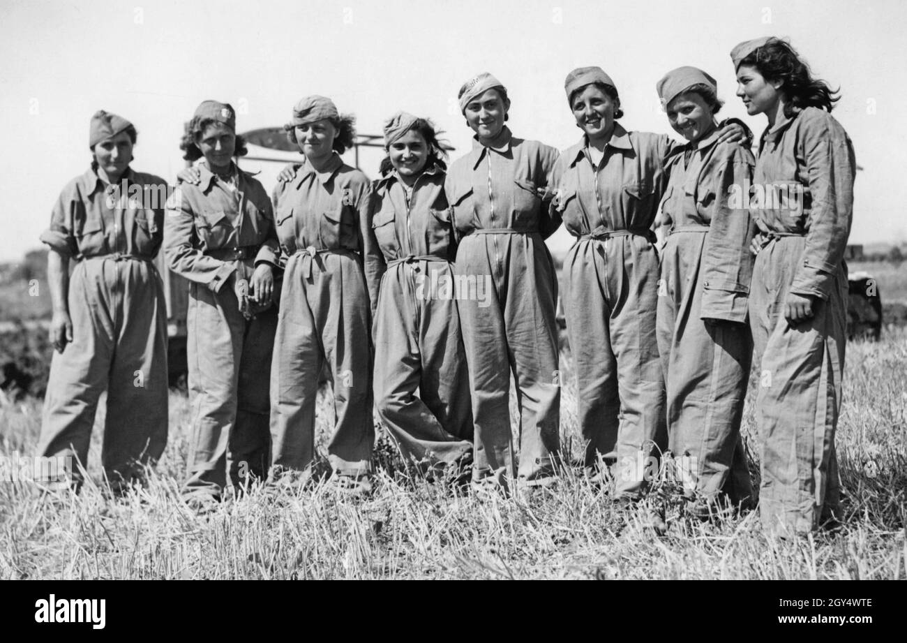 „Dieses Foto, aufgenommen am 20. Juli 1940 in der Nähe von Maccarese westlich von Rom, zeigt eine Gruppe junger italienischer Frauen in Arbeitskleidung auf einem geernteten Feld. Sie werden während der Ernte als Traktorfahrer in der Landwirtschaft eingesetzt, da viele Männer als Soldaten im Krieg sind. Für die faschistische Propaganda dienten Bilder wie diese als Beweis für die 'Mobilisierung von Frauenarbeit'. [Automatisierte Übersetzung]' Stockfoto