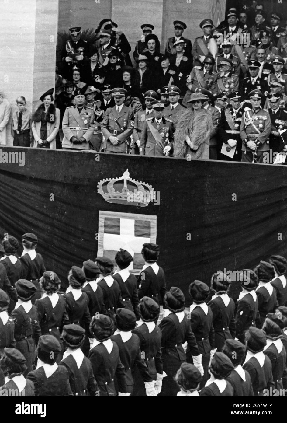 Adolf Hitler besuchte Anfang Mai 1938 Italien, verbündet mit Nazi-Deutschland. Am Freitag, den 6. Mai 1938, fand auf der Via Trionfale (heute Via di San Gregorio) in Rom eine Parade mit 50000 Soldaten und Mitgliedern faschistischer Organisationen statt. Das Bild zeigt Frauen der 'Giovani Fasciste', die an der Tribüne vorbeikommen. Auf der Tribüne befinden sich (von links nach rechts): Benito Mussolini, Adolf Hitler, König Viktor Emmanuel III. Von Italien und seine Frau Elena von Montenegro. Dahinter (2. Reihe, v.l.n.r.): Reichsaußenminister Joachim von Ribbentrop, italienischer Außenminister Graf Galeazzo Ciano (verdeckt), Stockfoto