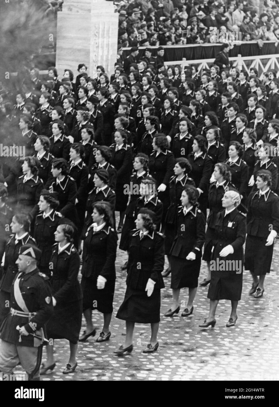 „eine Gruppe von Frauen einer faschistischen Organisation marschiert bei einer Parade an einer Tribüne in Rom vorbei, wobei ihre Augen nach rechts gerichtet sind. Die Frauen gehören vermutlich der Opera Nazionale del Dopolavoro an. Im Hintergrund das Publikum und eine Kolumne mit der Aufschrift ''SPQR''. Undatierte Fotografie, wahrscheinlich um das Jahr 1935 aufgenommen. [Automatisierte Übersetzung]' Stockfoto