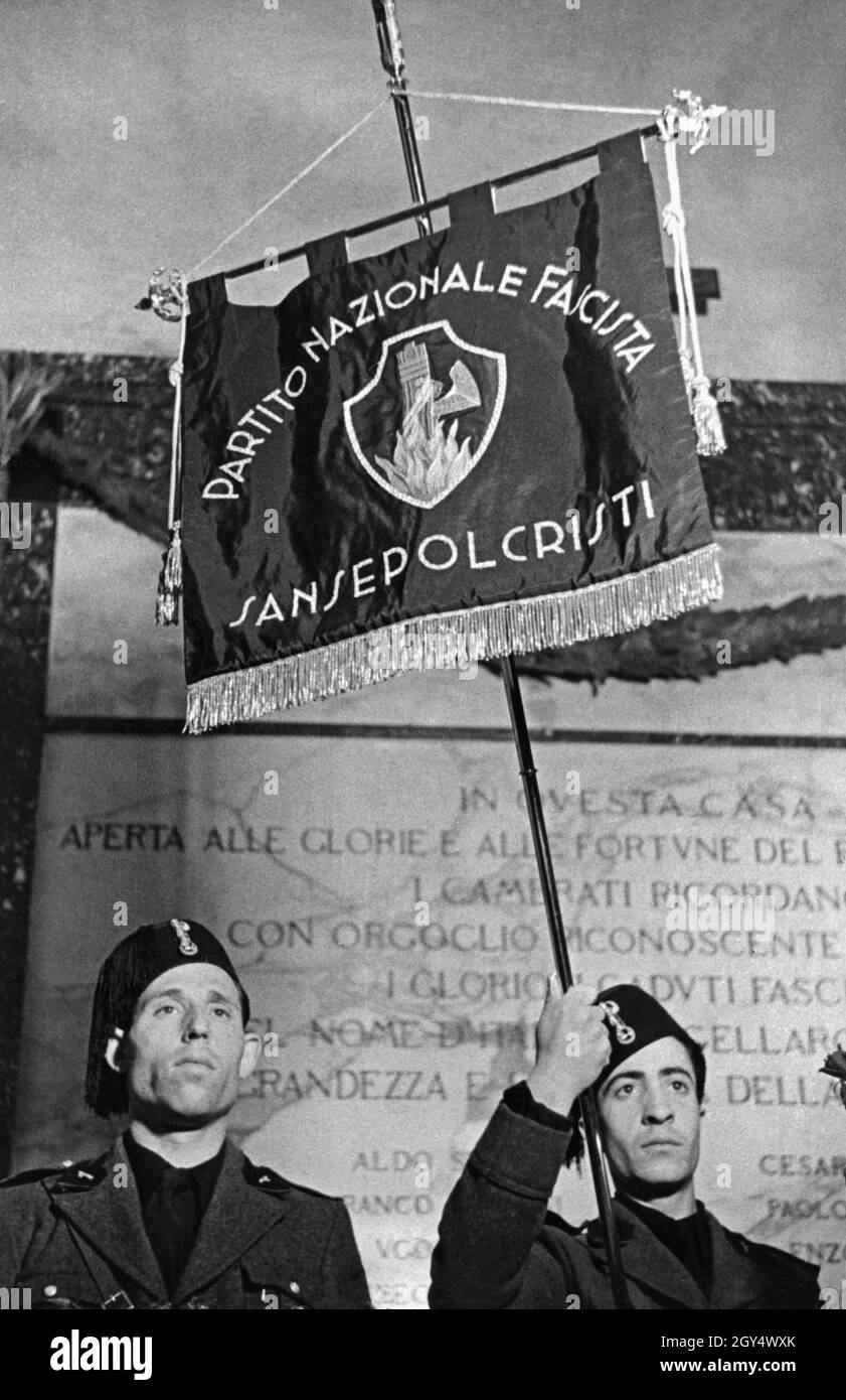 „ein Standardträger hält 1939 die 1. Sturmflagge der Partito Nazionale Fascista. Er steht vor einer Gedenktafel für die ''heroisch gefallenen Faschisten''. Auf der Flagge steht: ''Partito Nazionale Fascista / Sansepolcristi'', in der Mitte das Symbol der Faschisten, die Faschisten, die in einem Feuer brennen. [Automatisierte Übersetzung]' Stockfoto