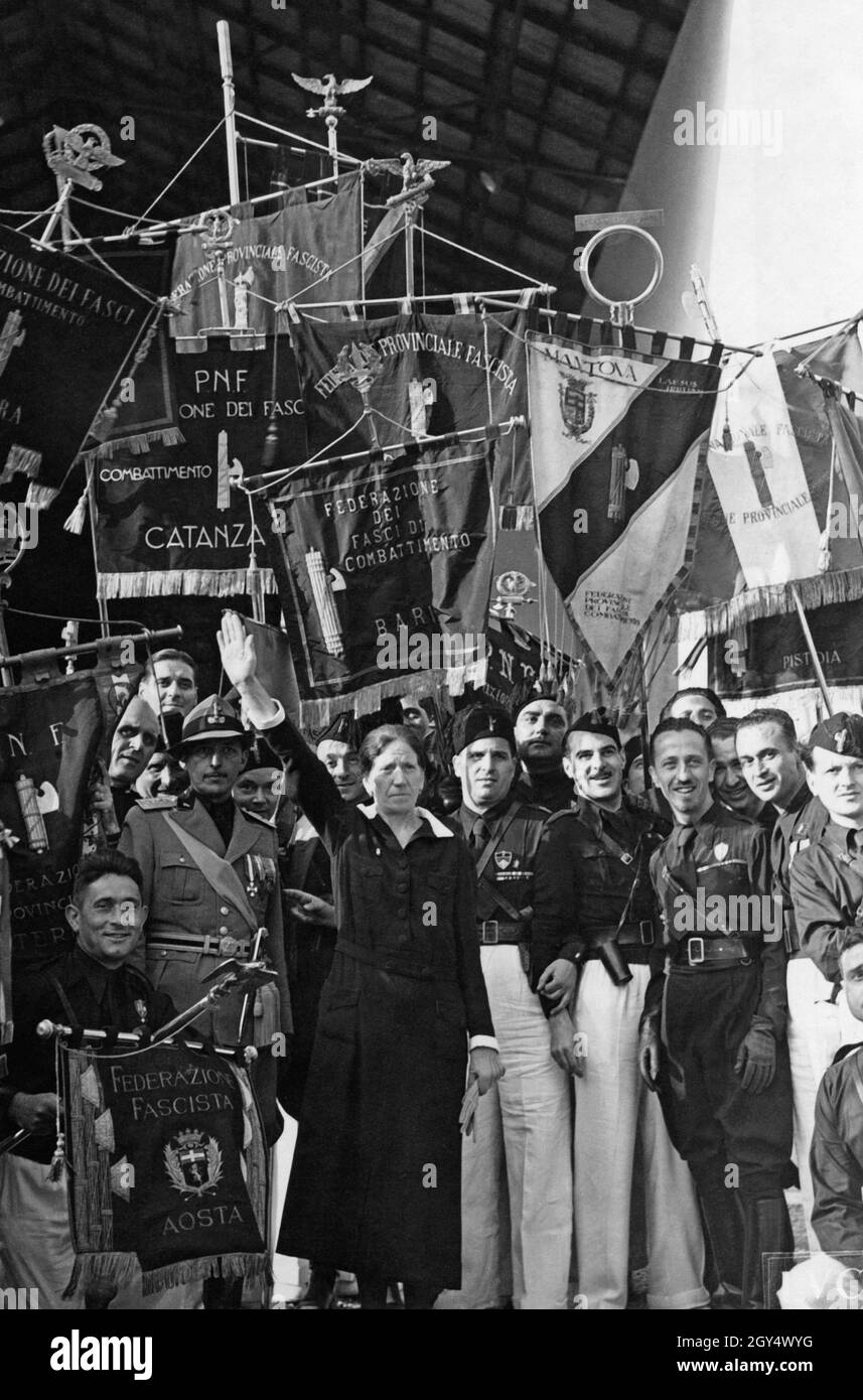 Das Foto aus dem Jahr 1937, aufgenommen in Genua, zeigt die Faschistin Teresa Cadella (Mitte, beim römischen Gruß den Arm hochhebende), eine einfache Frau aus dem Volk. Sie ist Schirmherrin des Panzerkreuzers Littorio, einem italienischen Schlachtschiff der Regia Marina. Auf dem Bild ist sie von Männern faschistischer Organisationen und lokaler Gruppen umgeben, darunter: Federazione Fascista, Combattimento Catanza, Federazione dei Fasci di combattimento Bari, Mantova und Pistoia. [Automatisierte Übersetzung] Stockfoto